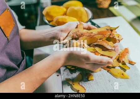 Pelures de pommes de terre dans les mains de la cuisinière femelle. Utilisation et transformation des déchets alimentaires, compostage, afin d'enrichir la fertilité des sols. Tri des ordures à la maison Banque D'Images