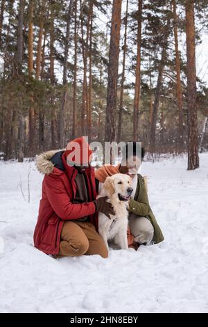 Un couple africain heureux embrasse son chien mignon lors de sa promenade dans la forêt en hiver Banque D'Images