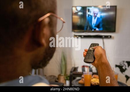 Gros plan d'un homme africain en lunettes à l'aide de la télécommande pour allumer les chaînes à la télévision pendant son temps libre à la maison Banque D'Images