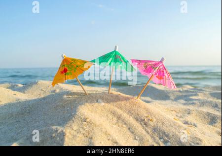 Trois parasols multicolores en papier sur une plage de sable avec ciel bleu Banque D'Images