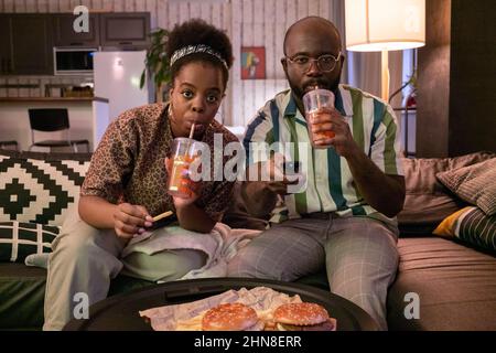 Un couple africain boit du soda et mange des frites pendant que vous regardez le film dans la chambre à la maison Banque D'Images