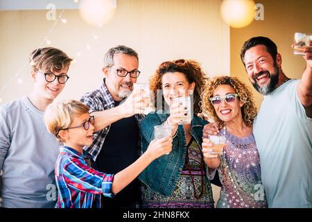 Un groupe d'amis heureux mêlant âges et générations célèbrent le toaster avec des boissons et en riant posant pour une photo. Joyeux adultes et garçons h Banque D'Images