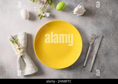 Table festive de Pâques avec assiette jaune, fleurs printanières et œufs verts colorés. Vue de dessus. Copier l'espace. Banque D'Images