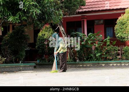 Lampung, Indonésie, décembre 17 2021- défoqué sur Une enseignante balayant la cour d'école le matin dans une école primaire Banque D'Images