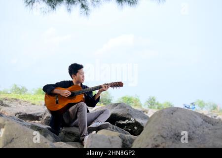 Lampung, Indonésie, février 12 2022- attention aux jeunes indonésiens jouant de la guitare sur la plage du village de Tridarmayoga, Lampung Indonésie Banque D'Images