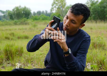 Lampung, Indonésie, février 12 2022- un indonésien est assis et tient un smartphone. Concept de style de vie Banque D'Images