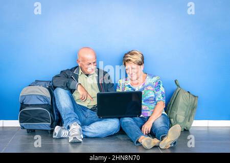 Heureux couple senior assis sur le sol avec ordinateur portable en attente d'un vol à l'aéroport - concept de personnes âgées actives et interaction avec le nouveau technolo Banque D'Images