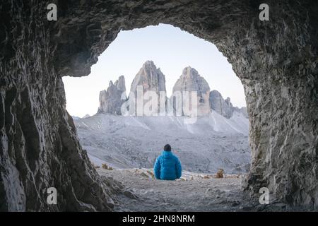 Tourisme en blouson bleu à la grotte de montagne contre trois sommets de Lavaredo, Alpes Dolomites, Italie, Europe. Photographie de paysage. Le Tre Cime Di Lavaredo culmine en arrière-plan Banque D'Images