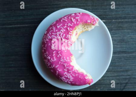 Vue de dessus à moitié mangé de beignet rose vif sur une assiette ronde blanche. Arrière-plan en bois vieilli. Objet isolé. Bonbons traditionnels américains pour le petit-déjeuner Banque D'Images