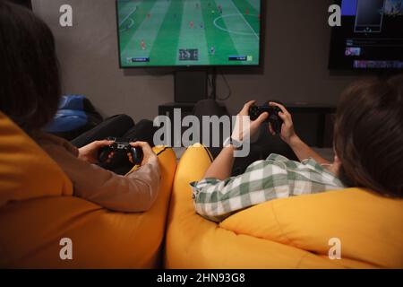 Vue arrière courte photo d'un couple jouant à des jeux vidéo ensemble, assis dans des chaises de sac de beanbag colorées Banque D'Images