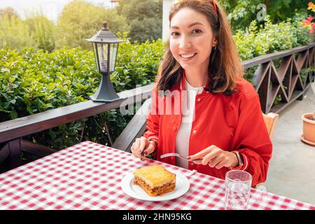 Une jeune fille souriante a une délicatesse grecque traditionnelle - moussaka. Il s'agit d'une casserole de fromage, de pommes de terre et de viande hachée à l'aubergine. Banque D'Images