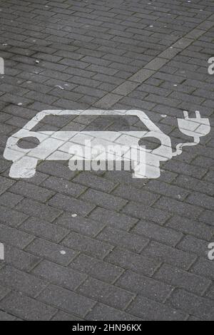 Symbole blanc d'une place de stationnement pour recharger les voitures électriques sur des pavés gris, mobilité verte (verticale), Kaiserslautern, Allemagne Banque D'Images