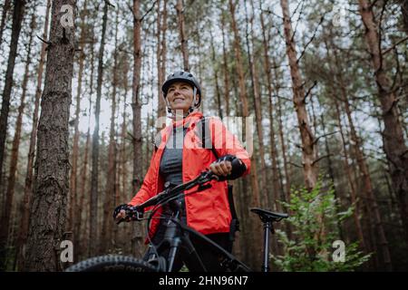 Vue à angle bas de la femme de vélo senior marchant et poussant le vélo à l'extérieur dans la forêt le jour de l'automne. Banque D'Images