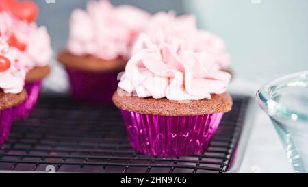 Vue rapprochée. Étape par étape. Piotage de crème de beurre italienne sur les cupcakes en velours rouge. Banque D'Images