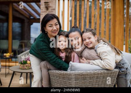 Deux sœurs heureuses avec mère et grand-mère embrassant et regardant la caméra à l'extérieur dans le patio en automne. Banque D'Images