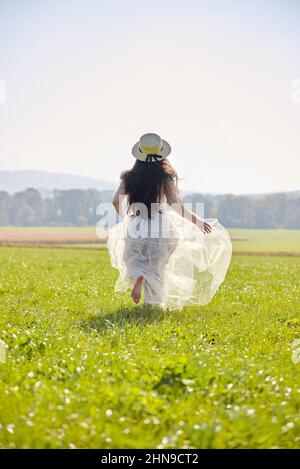 Jeune femme asiatique à cheveux longs et longs, vêtue d'une robe romantique lilas debout dans un champ d'herbe rétroéclairé Banque D'Images