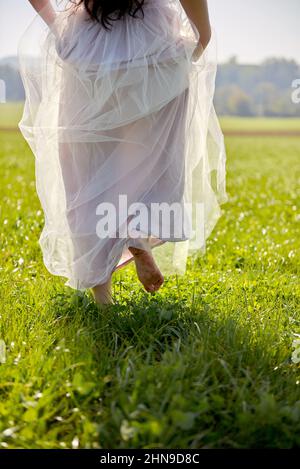 Jeune femme asiatique à cheveux longs et longs, vêtue d'une robe romantique lilas debout dans un champ d'herbe rétroéclairé Banque D'Images