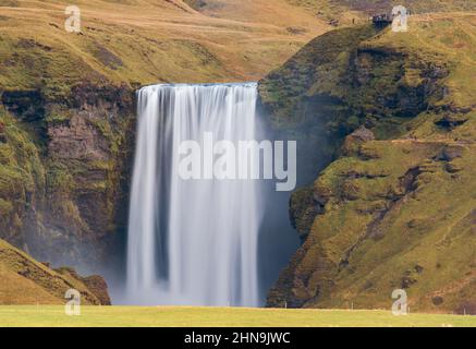 Longue exposition, cascade de Skogafoss depuis la distance avec les randonneurs sur le point de vue supérieur Banque D'Images