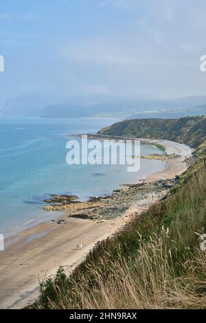 Deux personnes lointaines marchent le long de l'extrémité orientale de Porth Dinllaen Beach, au pays de Galles, par une journée lumineuse mais brumeuse. Banque D'Images