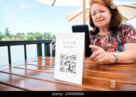 Femme hispanique mûre scannant un code QR avec son smartphone pour payer sa facture de restaurant à l'aide de la technologie sans contact et sans espèces. Focus sur la femelle cl Banque D'Images