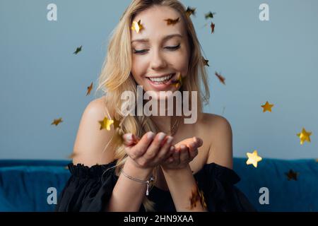 Jeune belle femme souriante avec de longs cheveux justes dans la robe noire avec les épaules cutaway attrapant des étoiles dorées brillantes. Banque D'Images