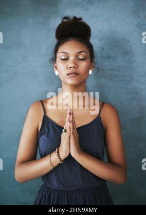 Trouver la paix intérieure. Photo courte d'une jeune femme méditant sur un fond gris. Banque D'Images