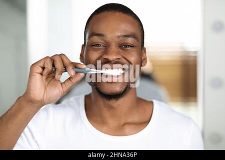 Joyeux Afro-américain Guy se brossant les dents avec brosse à dents à la maison Banque D'Images