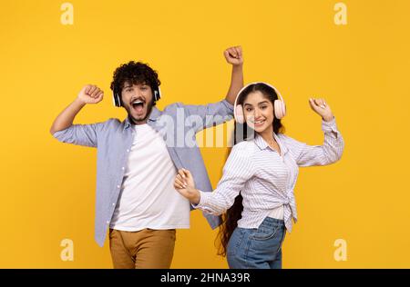 Amusez-vous et écoutez de la musique ensemble. Joyeux jeune couple indien dansant dans un casque, fond jaune Banque D'Images