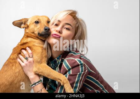 Une jolie jeune femme embrasse et embrasse son chien mongrel. Amour entre le propriétaire et le chien. Isolé sur fond blanc. Portrait de studio. Jeune fille embrassant nouveau charmant Banque D'Images