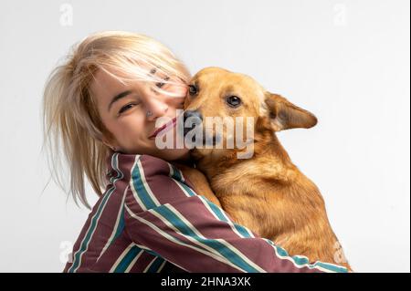 Une jolie jeune femme embrasse et embrasse son chien mongrel. Amour entre le propriétaire et le chien. Isolé sur fond blanc. Portrait de studio. Jeune fille embrassant nouveau charmant Banque D'Images