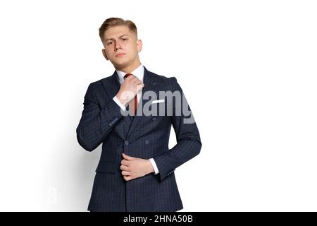 Élégant jeune homme d'affaires, étudiant, diplomate redresse sa cravate isolée sur fond blanc de studio. Émotions humaines, concept d'expression faciale. Banque D'Images