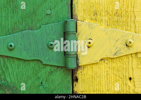 Gros plan de la charnière de porte en métal peinte en vert et jaune, plus rainures et marques de scie sur la surface des planches de bois. Banque D'Images