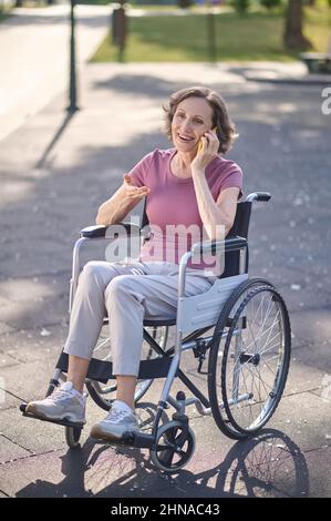 Femme souriante sur une chaise roulante parlant au téléphone Banque D'Images