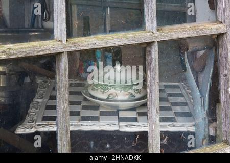 Plat en porcelaine antique avec couvercle sur le dessus de l'échiquier et vue à travers la fenêtre en verre de l'ancienne cabane rustique en bois. Banque D'Images