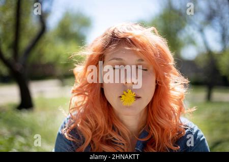 portrait d'une femme aux cheveux rouges avec une fleur dans sa bouche et des yeux fermés dans la nature Banque D'Images