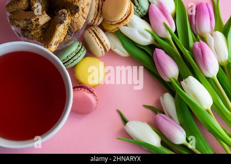 Vue imprenable sur la table basse dans la salle de séjour avec macarons français colorés et une tasse de thé décorée de fleurs de tulipe Banque D'Images