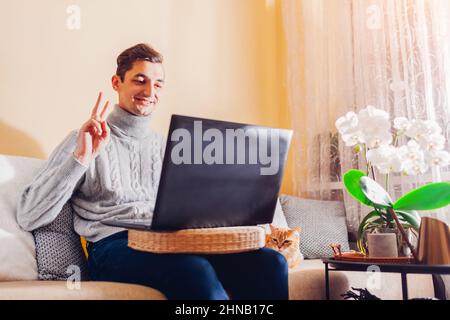 Homme chat vidéo en ligne depuis la maison avec un animal de compagnie utilisant un ordinateur portable. Guy appelle par ordinateur en faisant passer Bonjour. Communication sur Internet pendant le coronavirus covid lo Banque D'Images
