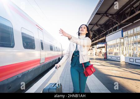 Belle fille courant et chassant le train de départ à la gare.Agitant la main et se précipitant pour se mettre sur - jeune femme d'affaires avec la valise de course Banque D'Images