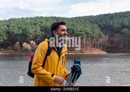 Un garçon avec un imperméable jaune debout devant le lac. Il a une chaise de camp sur sa main. Il aura un repos au bord du lac. Parc naturel sur un automne or Banque D'Images