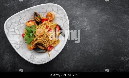 Spaghetti aux fruits de mer, pétoncles, crevettes, moules sur fond sombre avec espace pour le texte Banque D'Images