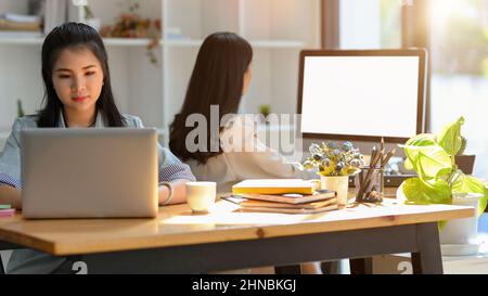 Deux femmes d'affaires concentrées travaillent sur leur ordinateur à leur bureau. Maquette d'écran blanc de l'ordinateur. Travailleurs d'agent Banque D'Images
