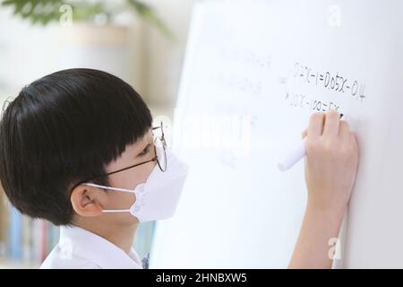 Un garçon élégant et mignon qui se concentre sur ses études tout en travaillant dur sur le tableau noir pour résoudre des problèmes mathématiques Banque D'Images