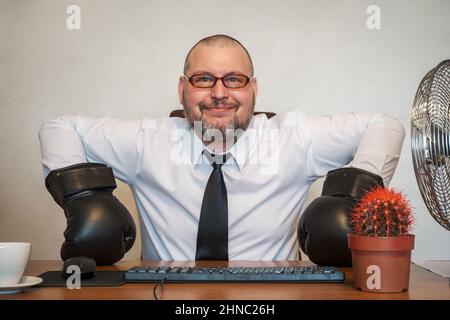 L'homme décrit comiquement le travail d'un homme d'affaires. Il est assis à une table portant des gants de boxe. Banque D'Images