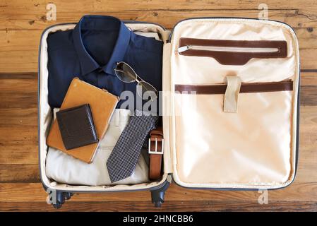 Entièrement emballé et prêt à l'emploi. Prise de vue en grand angle d'une valise remplie de divers éléments essentiels pour un homme d'affaires en voyage. Banque D'Images