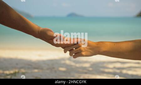 Mains de flirter jeune homme et femme touchant sur la plage dans l'ombre des palmiers contre calme azur océan vue proche. Voyager dans les pays tropicaux Banque D'Images