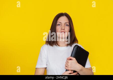 Portrait d'une femme dans un t-shirt blanc avec un ordinateur portable sur fond jaune. Femme d'affaires travaillant avec un ordinateur portable à la maison. Le concept de travail à distance ou Banque D'Images