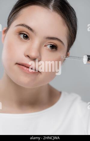 Portrait de la femme avec le syndrome de Down appliquant le sérum isolé sur le gris Banque D'Images