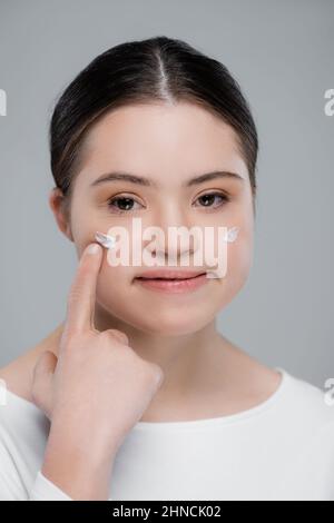 Femme avec le syndrome de Down pointant vers la crème sur le visage isolé sur le gris Banque D'Images