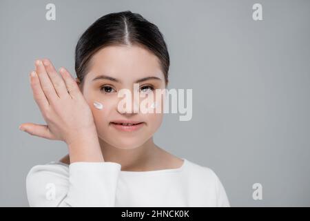 Femme positive avec le syndrome de Down et la crème du visage isolée sur le gris Banque D'Images