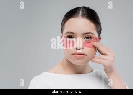 Jeune femme avec le syndrome de Down appliquant des taches oculaires isolées sur le gris Banque D'Images